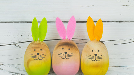 A group of three colorful Bunnies made out of wood in a row on white wooden background