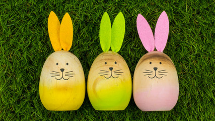 3 wooden bunnies with colorful ears lying next to each other on green grass