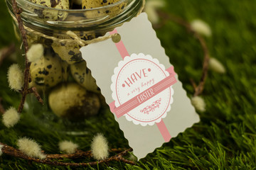 A Jar full of quail eggs standing on grass with pussy willow around it and a label saying have a very happy easter