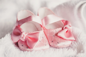 Fototapeta na wymiar Clothing for newborn. A pair of cute baby pink shoes with a bow for girls on a white bed.