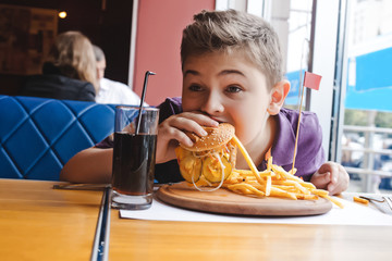 funny little boy eating a hamburger at a cafe, food concept