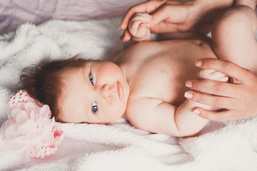 Close-up portrait of cute happy smiling baby girl lying down on bed. Mother is holding her newborn baby. Small daughter and mum.