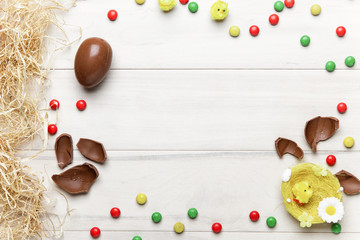 Easter chocolate egg with colorful explosion of candies and sweets on gray colored wooden background.