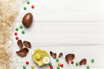 Easter chocolate egg with colorful explosion of candies and sweets on gray colored wooden background.