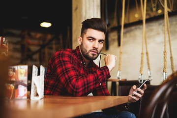 Hipster looking aside holding mobile phone.