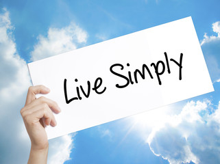 Live Simply Sign on white paper. Man Hand Holding Paper with text. Isolated on sky background