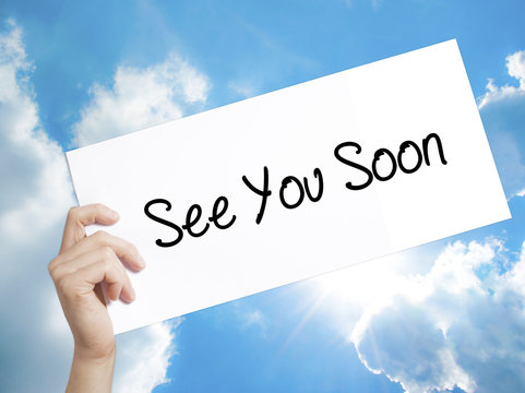 See You Soon Sign on white paper. Man Hand Holding Paper with text. Isolated on sky background.