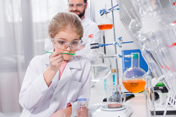 Smiling bearded teacher looking at little student making experiment in laboratory