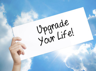Upgrade Your Life!  Sign on white paper. Man Hand Holding Paper with text. Isolated on sky background