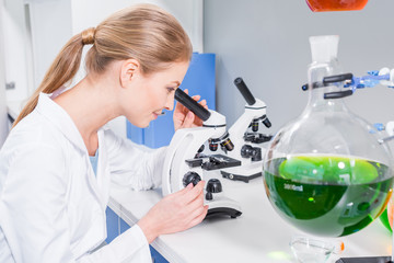 Side view of smiling young scientist working with microscope in chemical lab