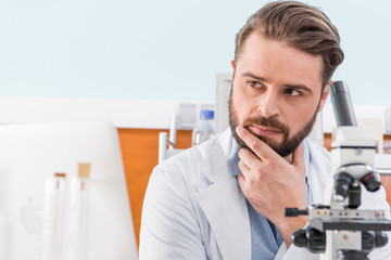 Naklejka na ściany i meble pensive bearded scientist working with microscope in laboratory