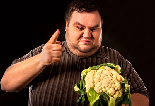 Diet fat man eating healthy food . Healthy breakfast with vegetables cauliflower for overweight person. Male trying to lose weight. Concept on black background.