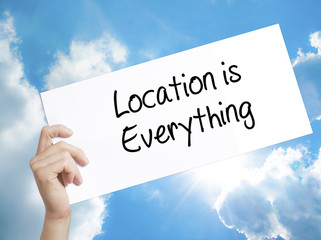 Location is Everything Sign on white paper. Man Hand Holding Paper with text. Isolated on sky background © netsay