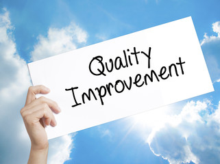 Quality Improvement Sign on white paper. Man Hand Holding Paper with text. Isolated on sky...