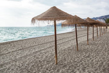 Straw parasols on empty beach. Nerja, Spain