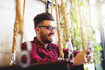 Handsome stylish man reading emails at smart phone smiling.