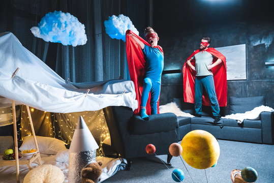 Father And Son In Red Superhero Costumes Playing At Home