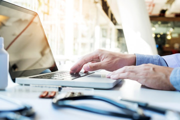 Close up of unknown female doctor sitting at the table near the window in hospital and typing at laptop computer