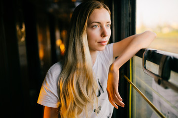 Photo of a very beautiful and attractive skinny teen girl with long hair in sleeveless shirt traveling by train alone on vacation and looking at window. Deep mood concept.