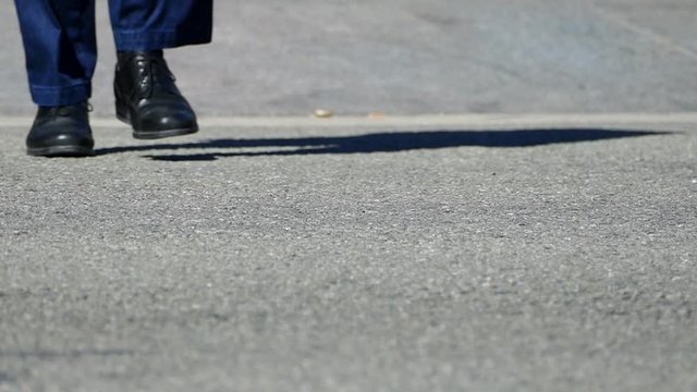 Detail of feet across a crosswalk, front view, with black shoes and blue jeans.Slow Motion.