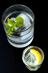Two cold cocktails with lemon and mint leaves, vertical on black background