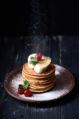 American pancakes on a plate with banana, cherry, mint and powdered sugar. Dark background. Vertical shot