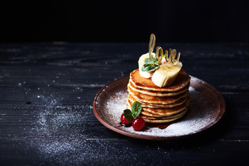 American pancakes on a plate with banana, cherry, mint, caramel syrop, love sign and sugar powder. Dark background.