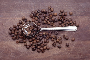 Silver spoon with coffee beans over wood background