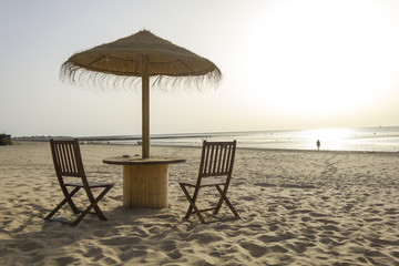 Wooden table and chairs with umbrella on the beach at sunset