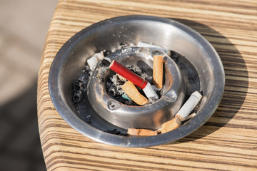 Silver ashtray with cigarette butts on a horeca table outside on a sunny day