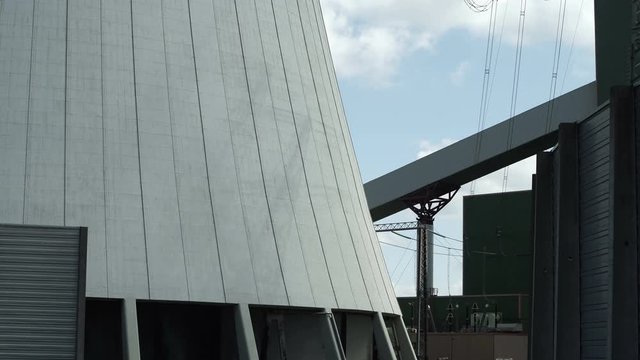 Light changes in industrial scene with the shadow showing the silhouette outline of an electricity tower or electrical pylon on the side of a hyperboloid cooling tower at a power generating station.