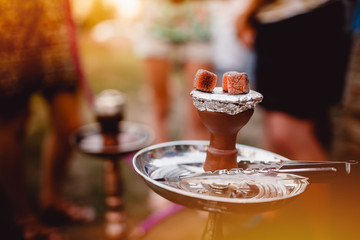 Red-hot coals for hookah against the background of group of friends. Conception is recreation on the landscape, campaign, camping, holidays