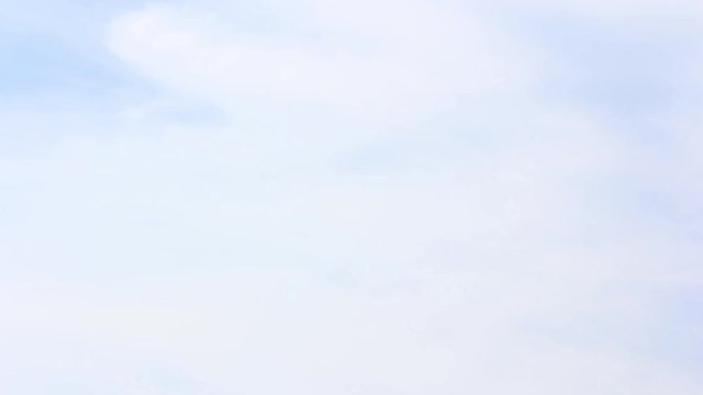 Time-lapse still of blue sky and clouds, showing a close-up view of the fluffy white formations drifting across a clear, bright background