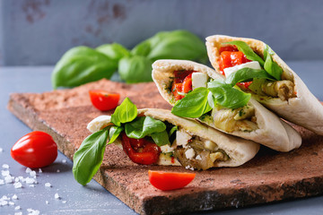 Pita bread sandwiches with grilled vegetables paprika, eggplant, tomato, basil and feta cheese served on terracotta board over gray stone background. Close up. Healthy fast food concept.