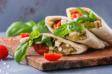 Pita bread sandwiches with grilled vegetables paprika, eggplant, tomato, basil and feta cheese served on terracotta board over gray stone background. Close up. Healthy fast food concept.