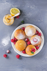 Homemade lemon muffin cupcakes with fresh raspberries, sugar powder, mint, served with jar of lemon curd and lemons over gray blue texture stone background. Top view with space.