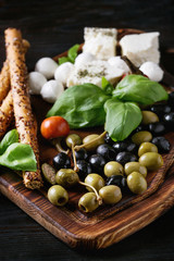 Mediterranean appetizer antipasti board with green black olives, feta cheese, mozzarella, capers, pepper, basil with grissini bread sticks over black wood burnt background. Close up © Natasha Breen
