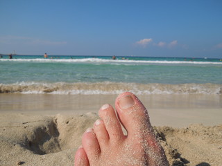 Foot of human on sand and soft wave on the sea