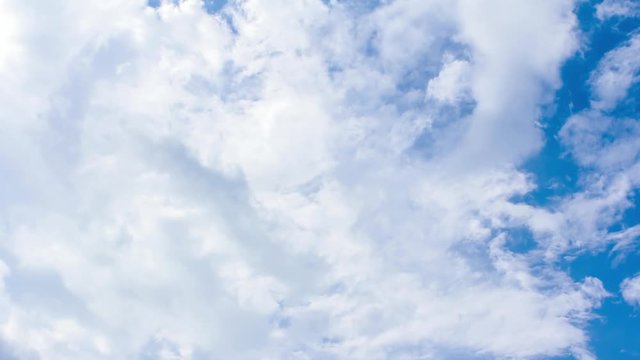 Time-lapse still of blue sky and clouds, showing a close-up view of the fluffy white formations drifting across a clear, bright background