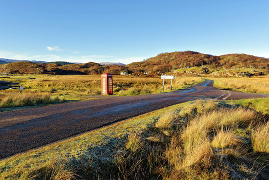 An autumn view of a red telephone box at the side of a quiet road in the remote Ardnamurchan moors of the Scottish Highlands, Scotland