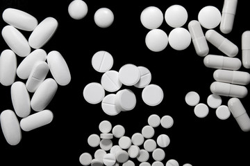Bunch of various white pills on black background