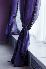 Purple curtains along window with a wide window sill. Day light, cool tones.