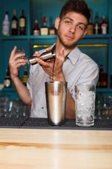 Young handsome barman pouring cocktail drink into glass