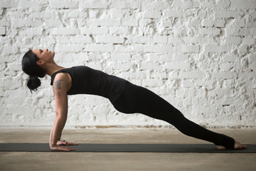 Young yogi attractive woman practicing yoga concept, stretching in Purvottanasana exercise, Upward Plank pose, working out, wearing sportswear, black tank top, pants, full length, loft background