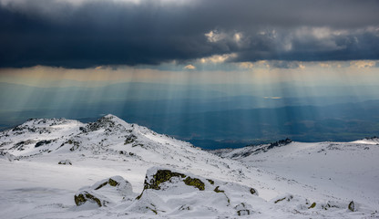 Sunny spells through thunderstorm clouds on a snowy mountain top