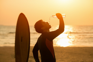 Vacation Concept ; Happy surfer drinking water with surfboards on the beach at sunset,Phuket,Thailand