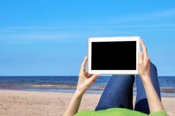Close up picture of female hands with tablet computer on a beach, black screen for copy space.