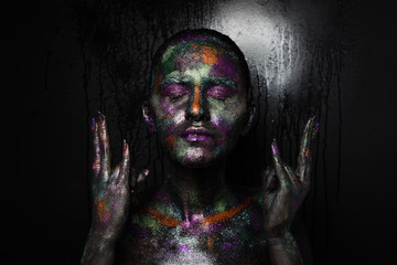 Young artistic woman in black paint and colourful powder. Glowing dark makeup. Creative body art on the theme of space and stars. Bodypainting project: art, beauty, fashion.