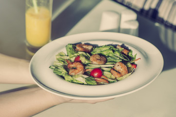 Female hands hold a plate with shrimp salad. The concept of eating and healthy lifestyles
