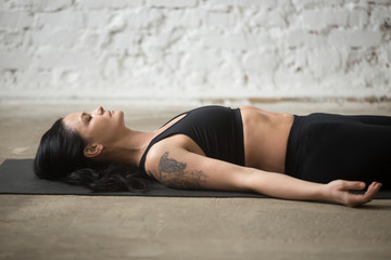 Fototapeta na wymiar Middle aged yogi woman practicing yoga concept, lying on floor in Savasana exercise, Corpse, Dead Body pose, working out, wearing sportswear, black top and pants, close up, white loft background